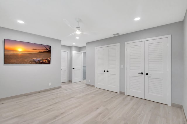 unfurnished bedroom with light wood-type flooring, two closets, and ceiling fan