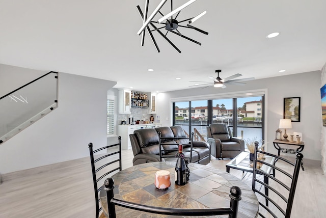 living room with bar, light hardwood / wood-style floors, ceiling fan, and a water view