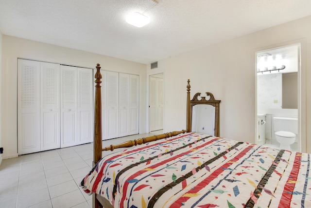 bedroom featuring light tile patterned floors, ensuite bath, a textured ceiling, and two closets