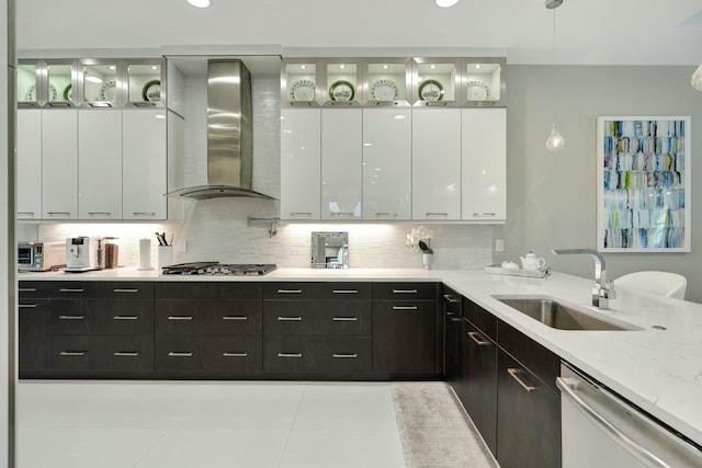 kitchen with wall chimney exhaust hood, sink, white cabinetry, light stone counters, and appliances with stainless steel finishes