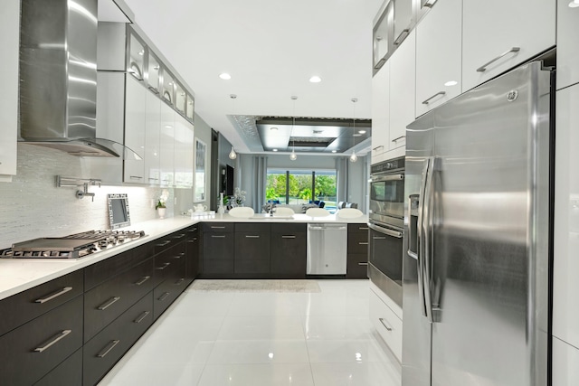 kitchen featuring wall chimney range hood, backsplash, stainless steel appliances, white cabinets, and light tile patterned flooring