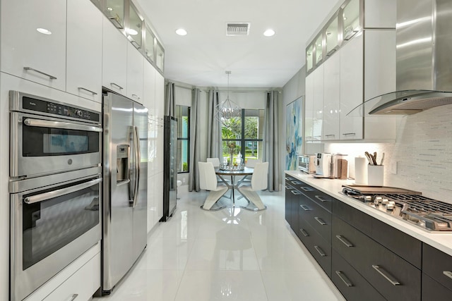 kitchen featuring white cabinetry, decorative backsplash, hanging light fixtures, stainless steel appliances, and wall chimney exhaust hood