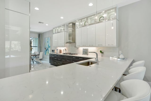 kitchen with decorative light fixtures, white cabinets, and wall chimney exhaust hood