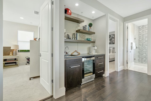 bar with wine cooler, dark brown cabinetry, dark wood-type flooring, and sink