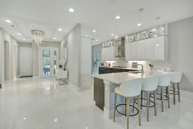 kitchen with pendant lighting, white cabinetry, sink, kitchen peninsula, and wall chimney range hood