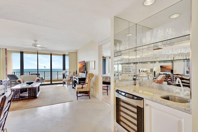 interior space featuring floor to ceiling windows, sink, beverage cooler, light stone countertops, and white cabinets