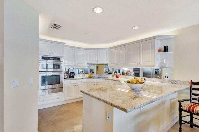 kitchen featuring appliances with stainless steel finishes, kitchen peninsula, white cabinets, and a kitchen bar