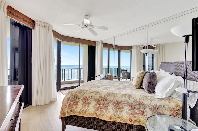 bedroom featuring light hardwood / wood-style flooring, access to outside, ceiling fan, and a water view