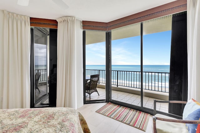 bedroom featuring multiple windows, wood-type flooring, a water view, and access to exterior