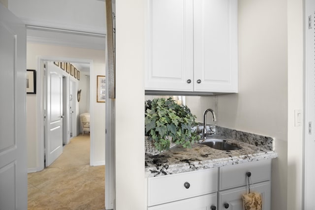 bar with light stone counters, sink, and white cabinets