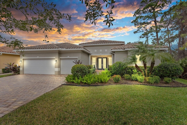 view of front facade featuring a tiled roof, a front yard, decorative driveway, and a garage