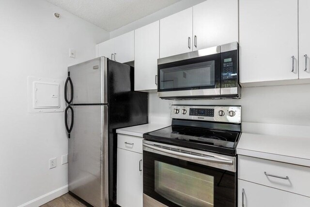 kitchen with white cabinetry, appliances with stainless steel finishes, wood-type flooring, and a textured ceiling