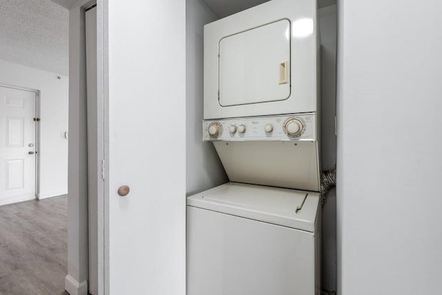 clothes washing area featuring light hardwood / wood-style flooring, stacked washer and clothes dryer, and a textured ceiling