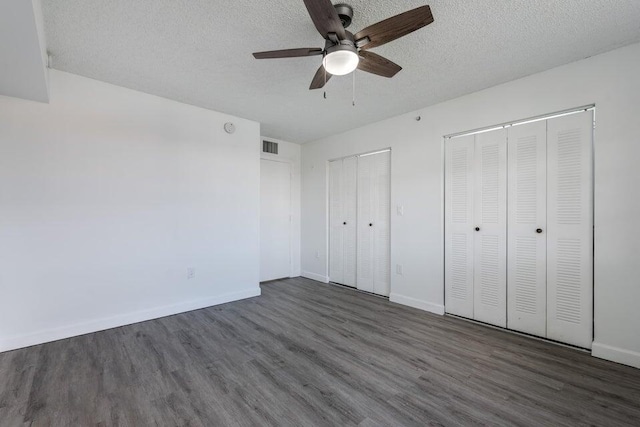 unfurnished bedroom featuring dark hardwood / wood-style floors, two closets, a textured ceiling, and ceiling fan