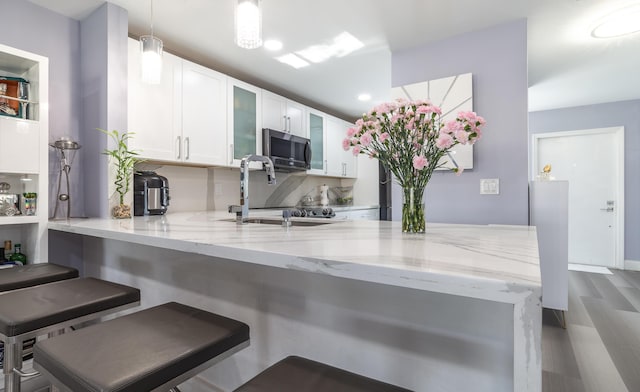 kitchen with decorative light fixtures, white cabinetry, kitchen peninsula, and a breakfast bar area