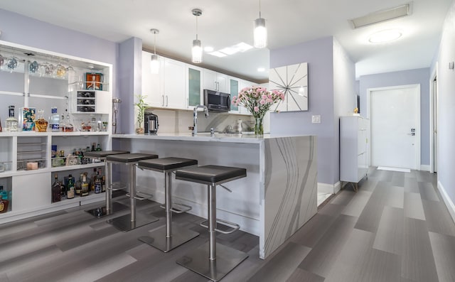 kitchen featuring white cabinets, decorative light fixtures, sink, kitchen peninsula, and a breakfast bar area