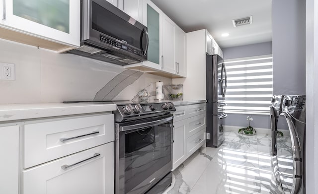 kitchen featuring light stone counters, white cabinets, washing machine and dryer, and appliances with stainless steel finishes