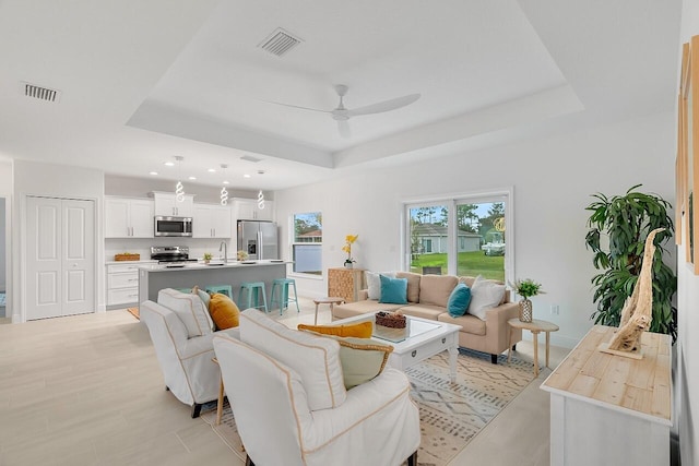 living area with recessed lighting, a raised ceiling, visible vents, and a ceiling fan