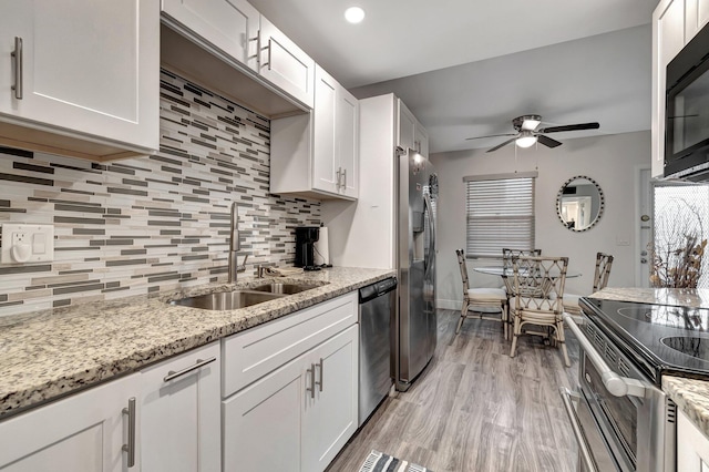 kitchen with appliances with stainless steel finishes, white cabinetry, sink, ceiling fan, and light stone counters