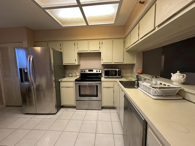 kitchen featuring sink, light tile patterned floors, stainless steel appliances, and cream cabinetry