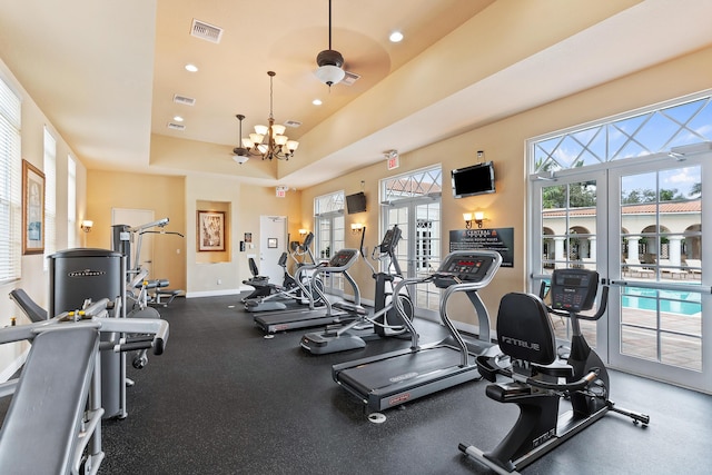 workout area featuring french doors, a raised ceiling, and a notable chandelier