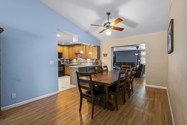 dining area featuring ceiling fan, sink, vaulted ceiling, and light hardwood / wood-style flooring