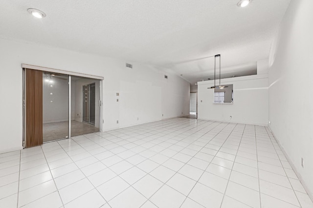 empty room with vaulted ceiling, a textured ceiling, and light tile patterned flooring