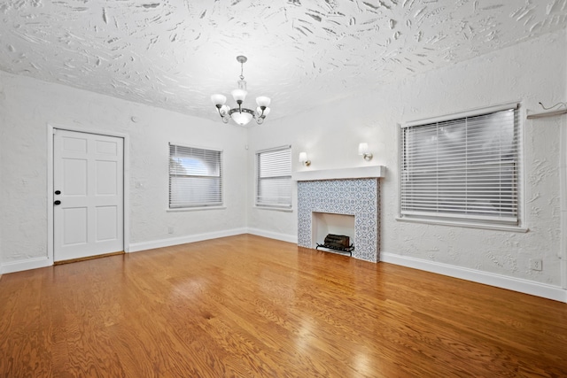 unfurnished living room featuring wood-type flooring, a tile fireplace, a textured ceiling, and a notable chandelier