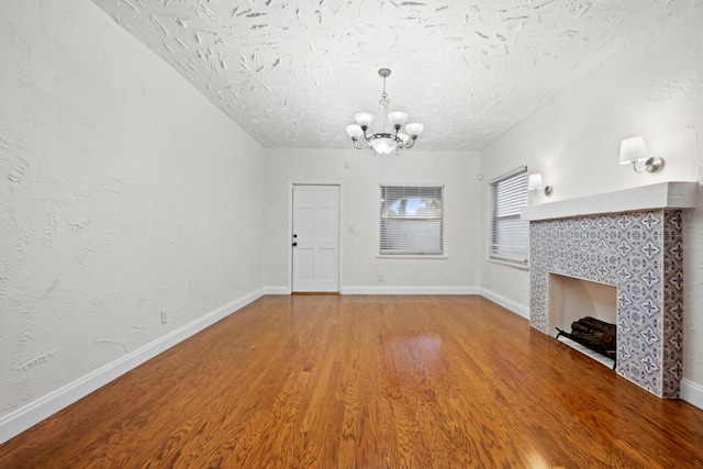 unfurnished living room with a notable chandelier, a tiled fireplace, a textured ceiling, and wood-type flooring