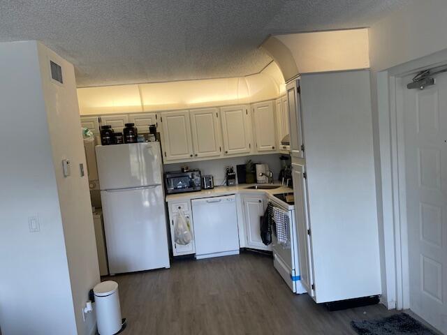 kitchen with sink, white appliances, dark hardwood / wood-style floors, a textured ceiling, and white cabinets