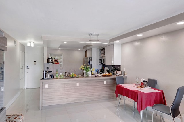 kitchen with light tile patterned flooring, a tray ceiling, kitchen peninsula, and white cabinets