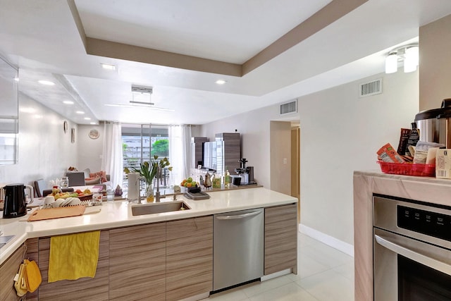 kitchen featuring appliances with stainless steel finishes, a tray ceiling, sink, and light tile patterned floors