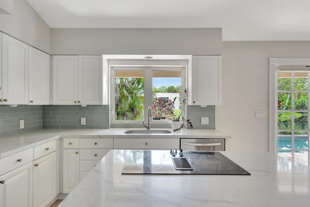 kitchen featuring tasteful backsplash, stainless steel dishwasher, sink, white cabinets, and light stone counters