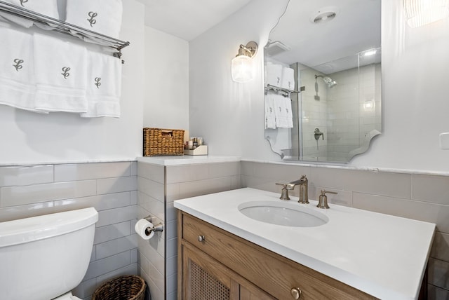 bathroom with a tile shower, tile walls, vanity, and toilet