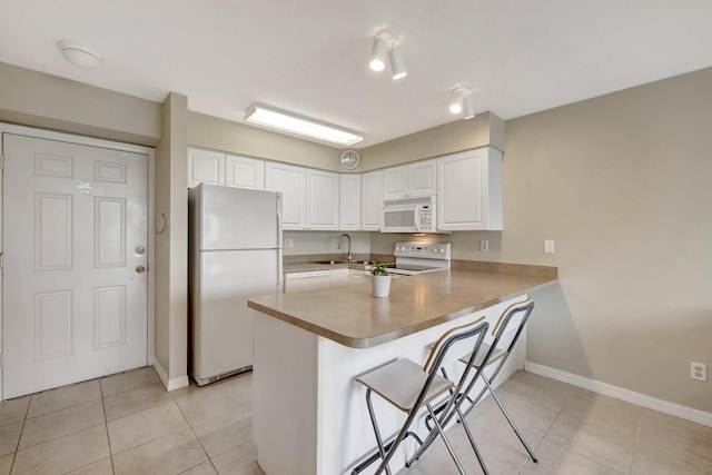 kitchen with light tile patterned floors, white cabinets, white appliances, a peninsula, and a kitchen bar