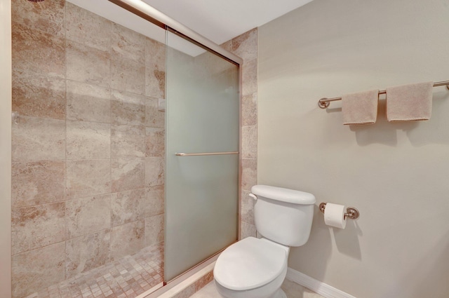 bathroom featuring toilet, a shower stall, and baseboards