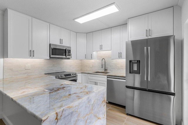 kitchen with sink, white cabinetry, light stone countertops, and appliances with stainless steel finishes