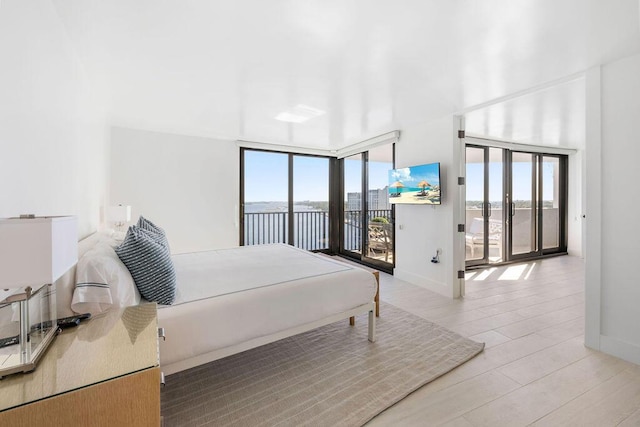 bedroom with a wall of windows, light wood-type flooring, and access to outside