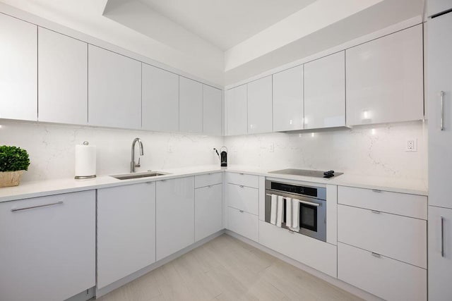 kitchen featuring sink, white cabinets, black electric cooktop, stainless steel oven, and decorative backsplash