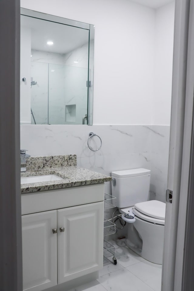 bathroom with tile walls, vanity, a shower with door, and toilet