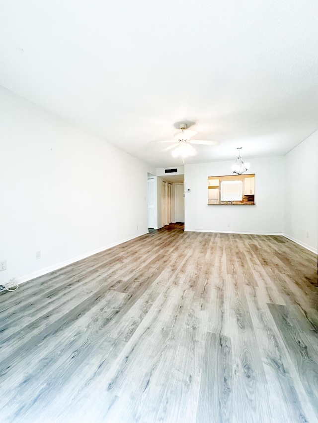 unfurnished living room with ceiling fan with notable chandelier and light hardwood / wood-style flooring