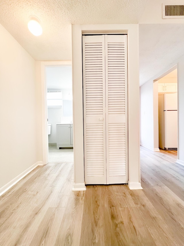 corridor with light wood-type flooring and a textured ceiling