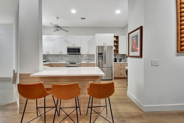 kitchen featuring appliances with stainless steel finishes, a kitchen breakfast bar, kitchen peninsula, decorative backsplash, and white cabinets