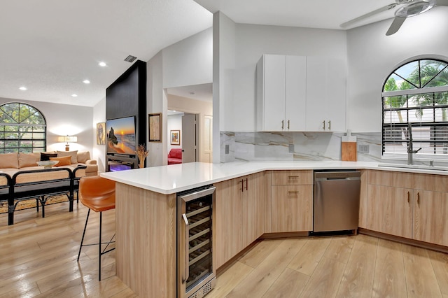 kitchen featuring wine cooler, a breakfast bar area, white cabinetry, stainless steel dishwasher, and kitchen peninsula