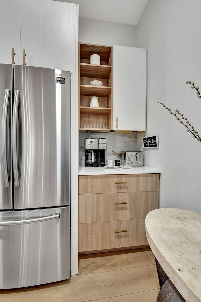 kitchen featuring white cabinetry, stainless steel fridge, decorative backsplash, light brown cabinets, and light wood-type flooring