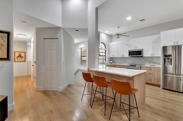 kitchen featuring white cabinetry, a kitchen breakfast bar, decorative backsplash, a center island, and stainless steel appliances