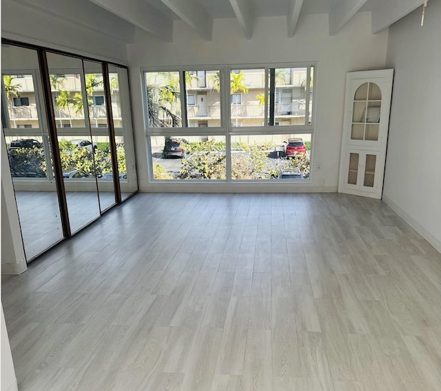 unfurnished room featuring beamed ceiling, a healthy amount of sunlight, and light hardwood / wood-style flooring