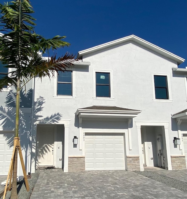 view of front facade featuring stone siding, stucco siding, decorative driveway, and a garage