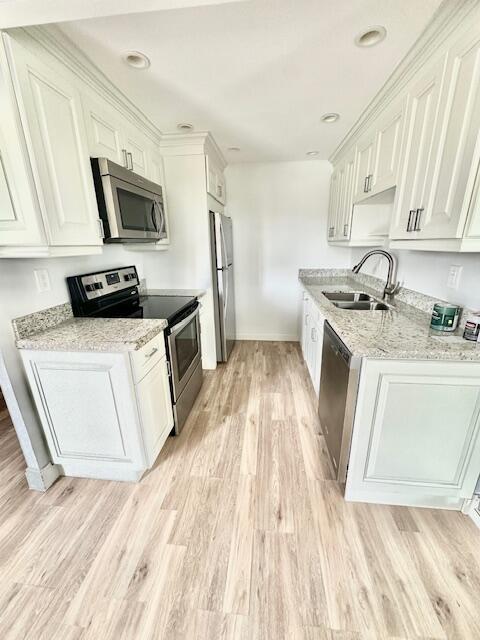 kitchen featuring stainless steel appliances, white cabinetry, sink, and light hardwood / wood-style flooring