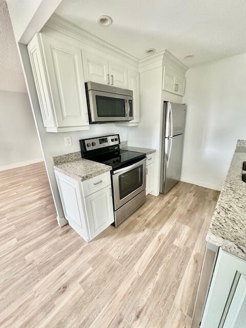 kitchen with stainless steel appliances, white cabinetry, light wood-type flooring, and light stone counters